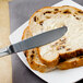 A Walco stainless steel butter knife spreading butter on a piece of bread.