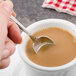 A person holding a Walco stainless steel demitasse spoon over a cup of coffee.