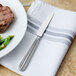 A Walco stainless steel dinner knife on a napkin next to a steak