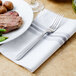 A Walco Maremma stainless steel fork on a white napkin next to a plate of meat and vegetables.
