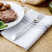 A Walco Freya stainless steel long European table fork on a plate with meat.