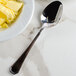 A Walco Prim stainless steel serving spoon next to a bowl of butter on a counter.