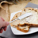 A hand holding a Walco Prim stainless steel butter spreader over a piece of bread with butter.