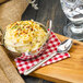 A bowl of mashed potatoes on a wooden tray with a Walco Maremma stainless steel teaspoon.
