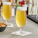 Two Acopa stemmed Pilsner glasses of beer sit on a table next to a bowl of nuts.