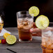 A hand holding an Arcoroc highball glass of iced tea with a lime slice and a spoon in a lemon.