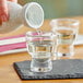 A person pouring sake into an Acopa Select sake shot glass on a table.