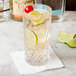 A Arcoroc highball glass of water with lime and cherry and lime slices.