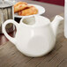 A white Tuxton China teapot on a table.