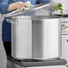 A person using a white towel to cover a Vigor SS1 Series stainless steel stock pot on a stove.