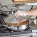 A person wearing gloves using a Vigor stainless steel saute pan to cook food with a lid on it.