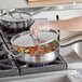 A person using a Vigor stainless steel saute pan with food in it.