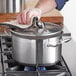 A person holding a Vigor stainless steel sauce pot with a towel over a stove.