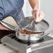 A person using a Vigor stainless steel saute pan to cook food on a stove.