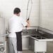 A man in a white shirt and black apron installing a Regency stainless steel 3 compartment corner sink with drainboards.