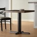 A Lancaster Table & Seating black cast iron table base with a wooden table top and two chairs.