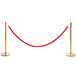 A Lancaster Table & Seating gold rope-style crowd control stanchion with red rope between two gold poles.