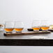 A group of Reserve by Libbey Kentucky Bourbon Trail tasting glasses filled with brown liquid on a wooden table.