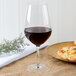A Chef & Sommelier Sequence Bordeaux wine glass filled with red wine on a table with a plate of pasta.