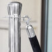 A Lancaster Table & Seating silver crowd control stanchion with black rope.