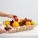 A hand holding an apple in a Tablecraft rectangular woven basket full of fruit.