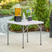 A Lancaster Table & Seating granite white folding table with a drink dispenser and flowers on it.