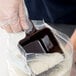 A person using a Carlisle brown polycarbonate portion scoop to fill a plastic bag with rice.