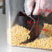 A plastic gloved hand using a Carlisle brown polycarbonate portion scoop to measure macaroni.