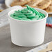 A Choice white paper food cup with green ice cream and a wooden spoon on a napkin.