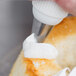 A person using an Ateco St. Honore piping tip on a pastry bag to pipe white frosting on a piece of cake.