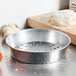 An American Metalcraft aluminum pizza pan with holes in it on a counter with dough and tomatoes.