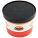 A white paper soup container with an orange and black design and a black vented lid.