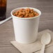 A white double poly-coated paper food cup filled with beans on a table with a spoon.