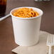 A white Choice paper food cup filled with spaghetti on a table with a fork.