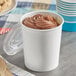 A close-up of a Choice white paper food cup with chocolate ice cream inside and a wooden spoon on the counter.