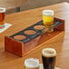 An Acopa walnut flight carrier holding four beer glasses on a wooden table in a brewery tasting room.