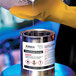 A person pouring liquid onto a metal can using Avery UltraDuty GHS chemical labels.