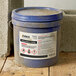 A blue bucket of dirt with a blue lid on top of Avery UltraDuty GHS Labels.