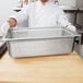 A chef holding a Choice stainless steel perforated hotel pan on a counter.