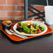 A Vollrath orange plastic fast food tray holding a plate of salad with a muffin on it.