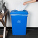 A person putting paper in a Lavex blue recycling bin with a blue lid and a slot.