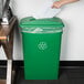 A person putting paper into a Lavex green rectangular recycling bin with a green lid and a slot.