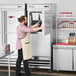A man in a professional kitchen opening an Avantco stainless steel solid half door reach-in freezer.
