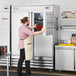 A man in an apron standing in front of an Avantco stainless steel reach-in refrigerator.