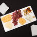 An American Metalcraft white flat melamine platter with cheese, grapes, and crackers on it.