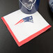 A New England Patriots beverage napkin with a logo on a table next to a can.