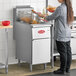 A woman using an Avantco natural gas floor fryer to cook food in a commercial kitchen.