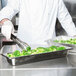 A chef in a white coat using a Vollrath Miramar decorative food pan to prepare broccoli.