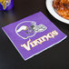 A Creative Converting Minnesota Vikings luncheon napkin with a helmet logo on it next to a plate of chicken wings.