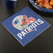 A New England Patriots luncheon napkin on a table with a plate of food.
